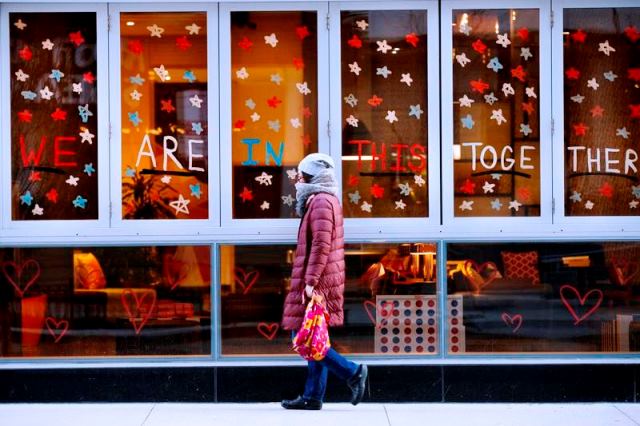 A woman walks by restaurant windows with the words WE ARE IN THIS TOGETHE written outside the Aloft hotel in the Gold Coast neighborhood on April 1, 2020, in Chicago. (Armando L. Sanchez - Chicago Tribune)